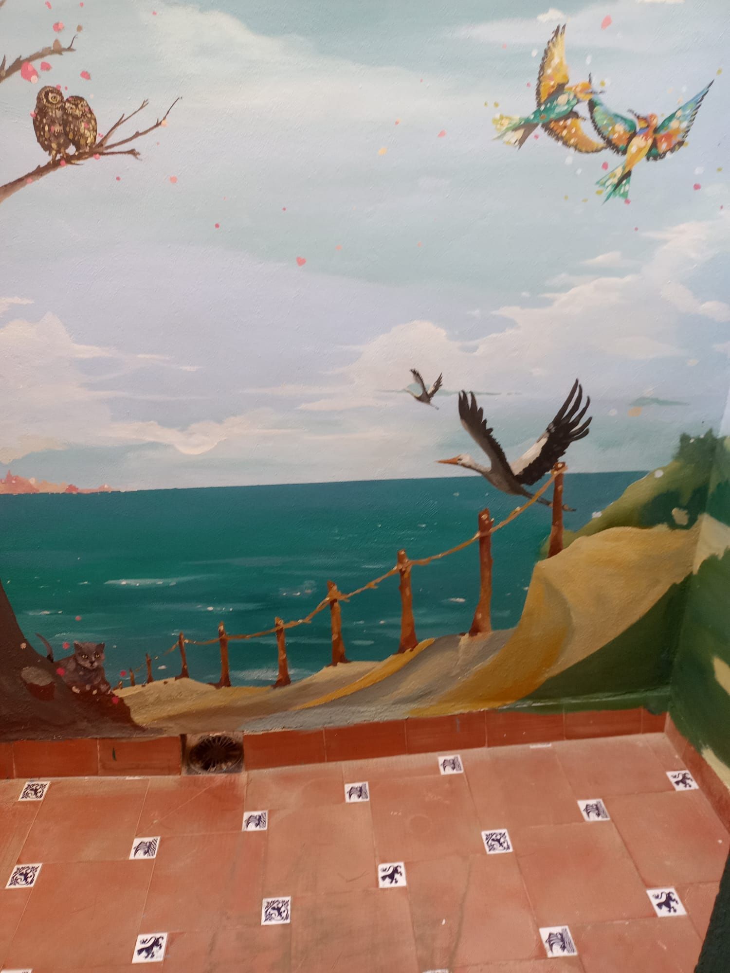 Mural de un acantilado costero con pájaros, el océano, una valla de cuerda y un suelo de baldosas en primer plano.