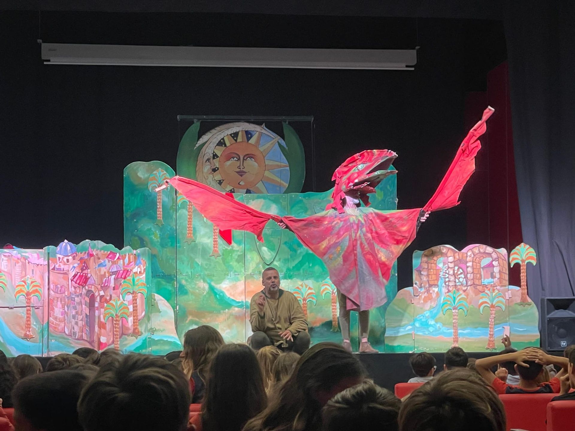 Espectáculo escénico lleno de color con una gran marioneta de dragón de alas rosas y un artista sentado en el centro.