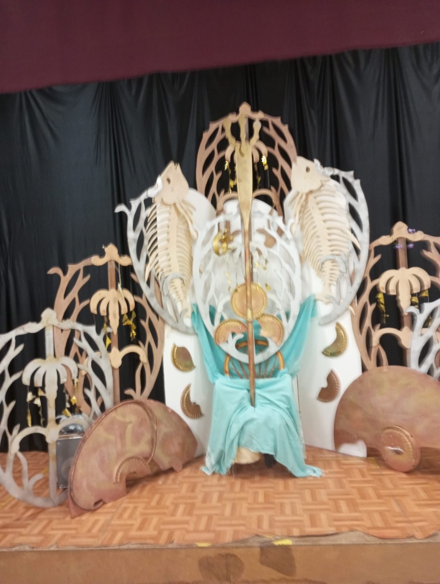 Fondo decorativo para el escenario con esculturas de esqueletos, cortinas turquesas y accesorios redondos marrones sobre un suelo estampado.