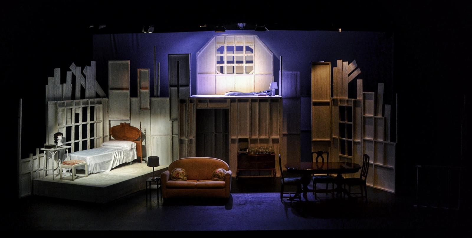 Escenario decorado con una escena de dormitorio: cama, cómoda, sofá, sillas y una ventana bajo iluminación violeta.