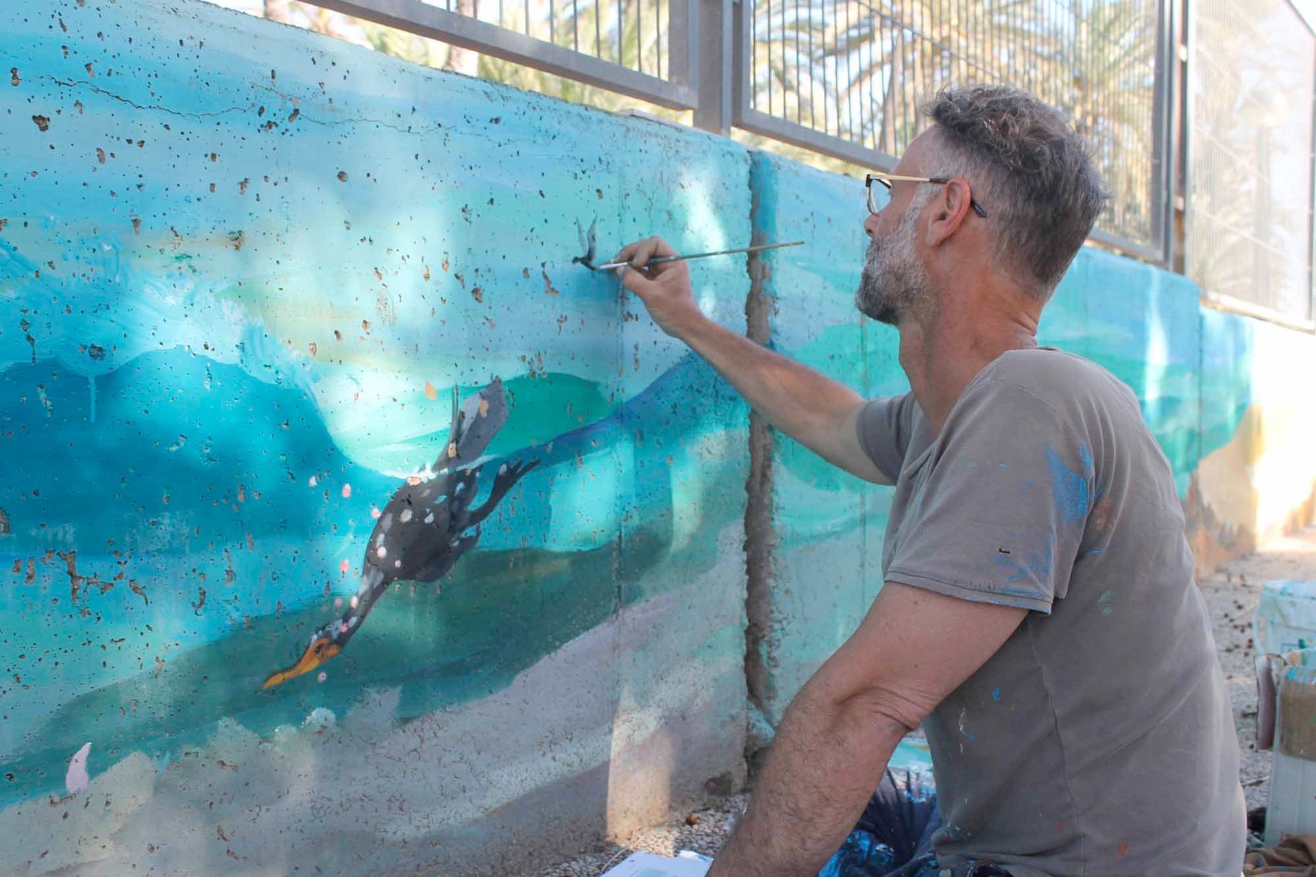 Un hombre está pintando un cuadro de un pájaro en una pared.