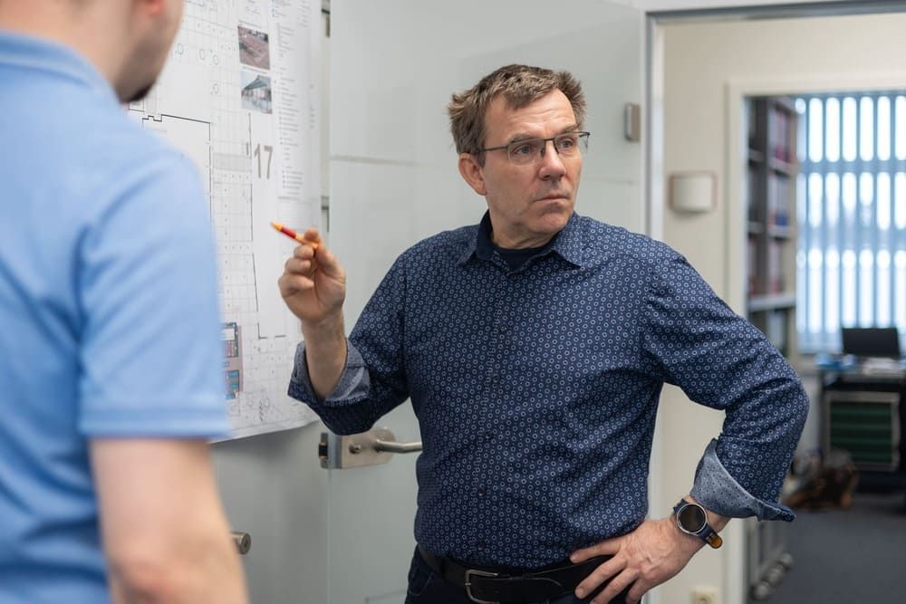 Ein Mann steht vor einem Whiteboard und spricht mit einem anderen Mann.