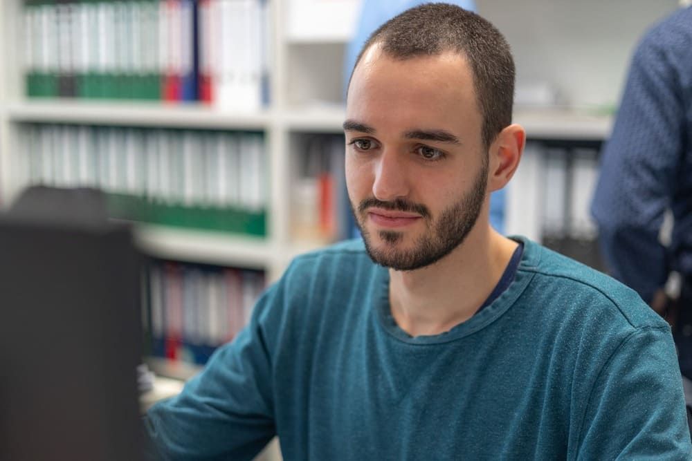 Ein Mann mit Bart sitzt an einem Schreibtisch vor einem Computer.