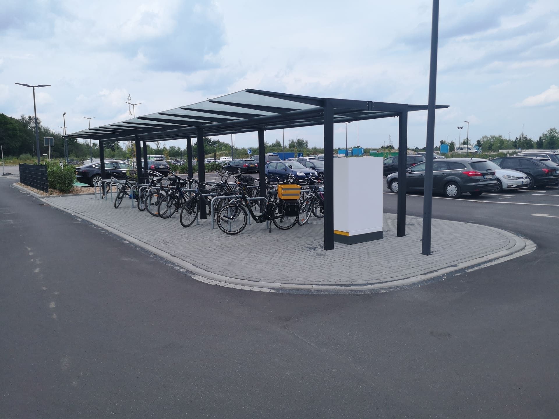 Auf einem Parkplatz ist eine Reihe Fahrräder unter einem Vordach abgestellt.