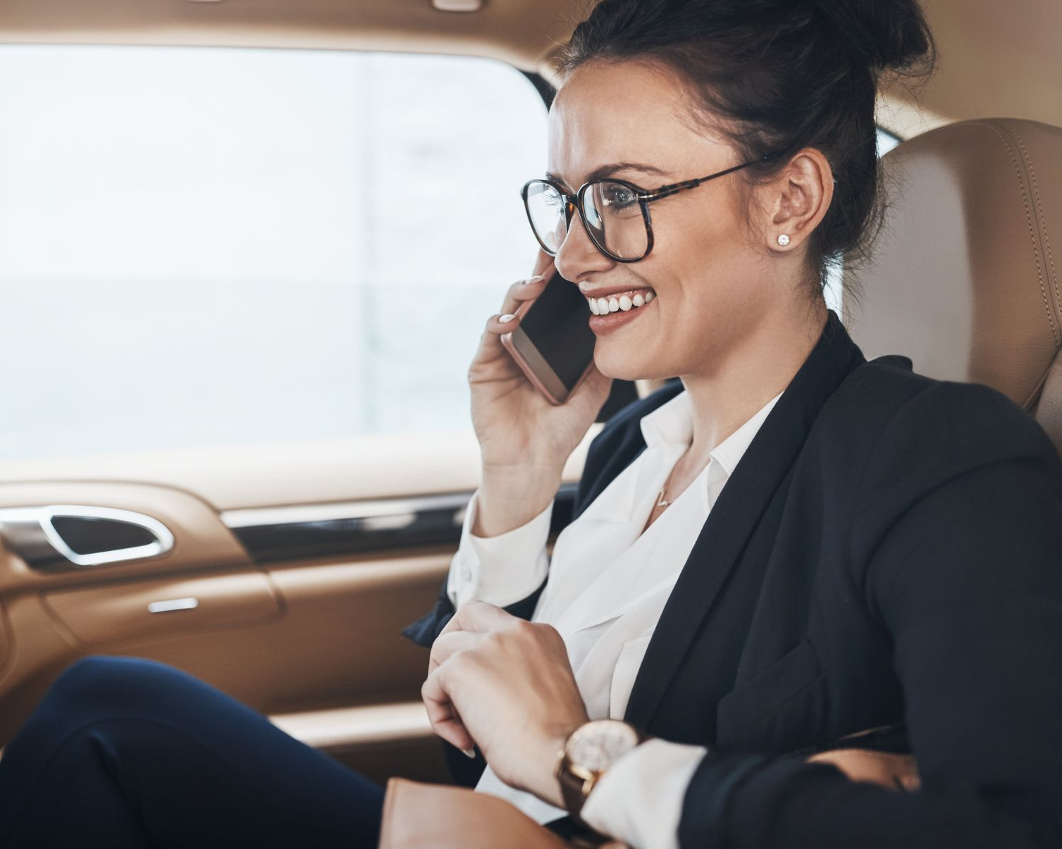 Un professionnel souriant portant des lunettes parle au téléphone avec un smartphone à l'intérieur d'une voiture.