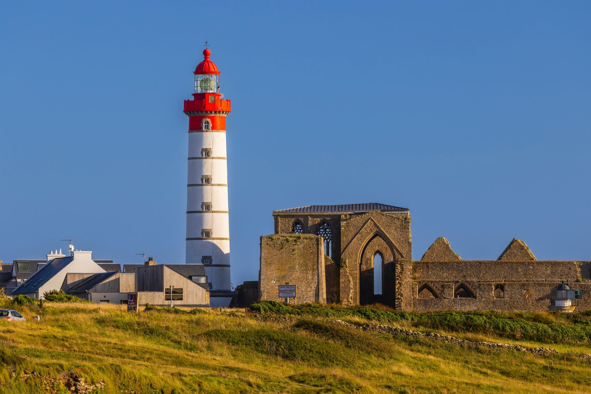 Phare surplombant des ruines de pierre sur une colline côtière.