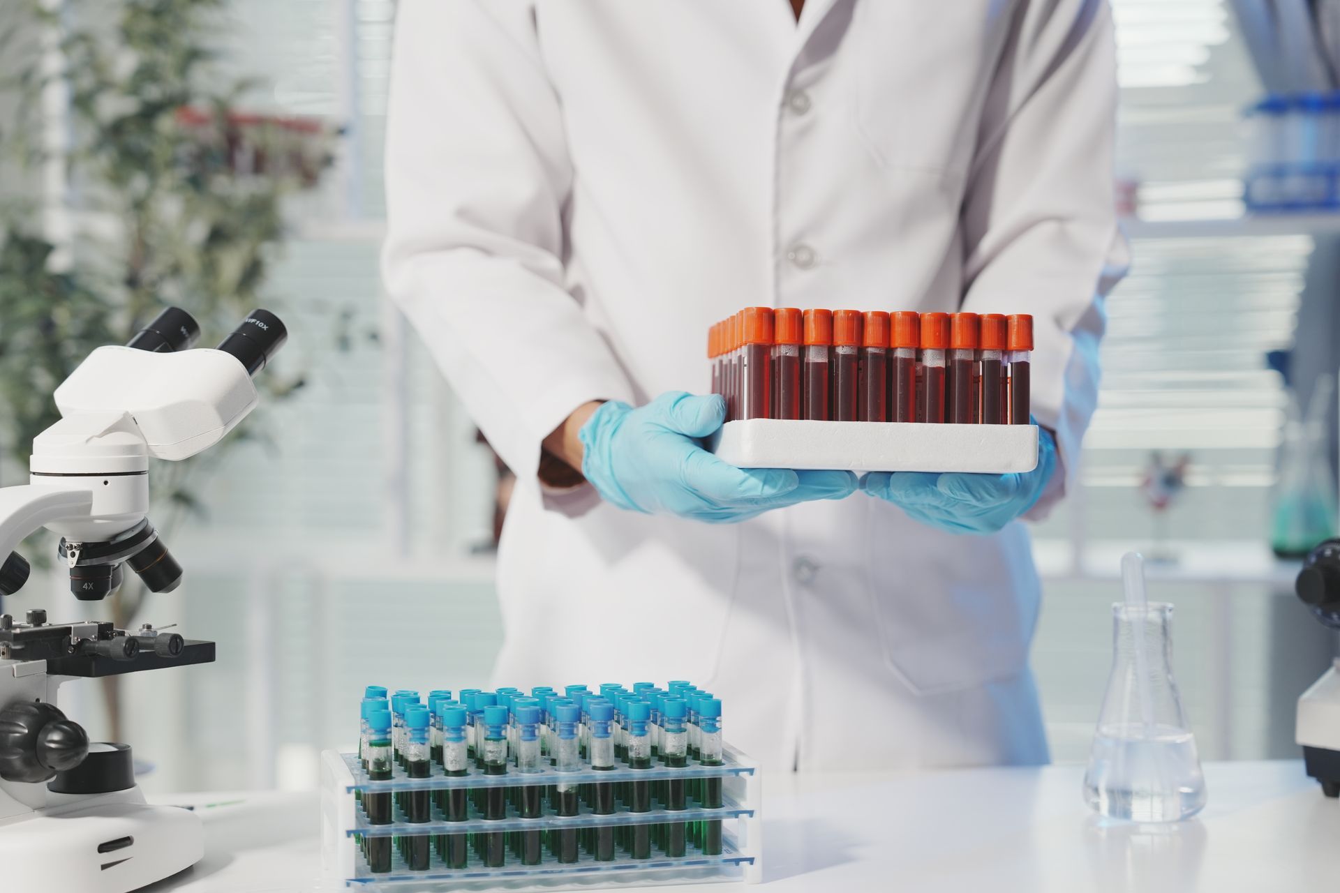 Technicien de laboratoire en blouse et gants tenant des tubes à essai dans un laboratoire.