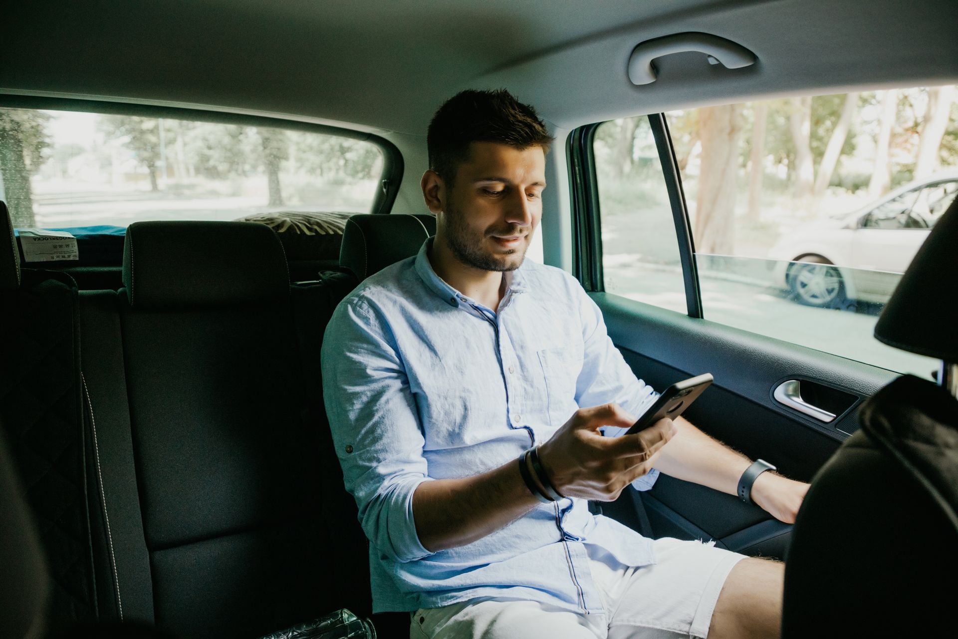 Un homme assis à l'arrière d'une voiture, regardant un smartphone.