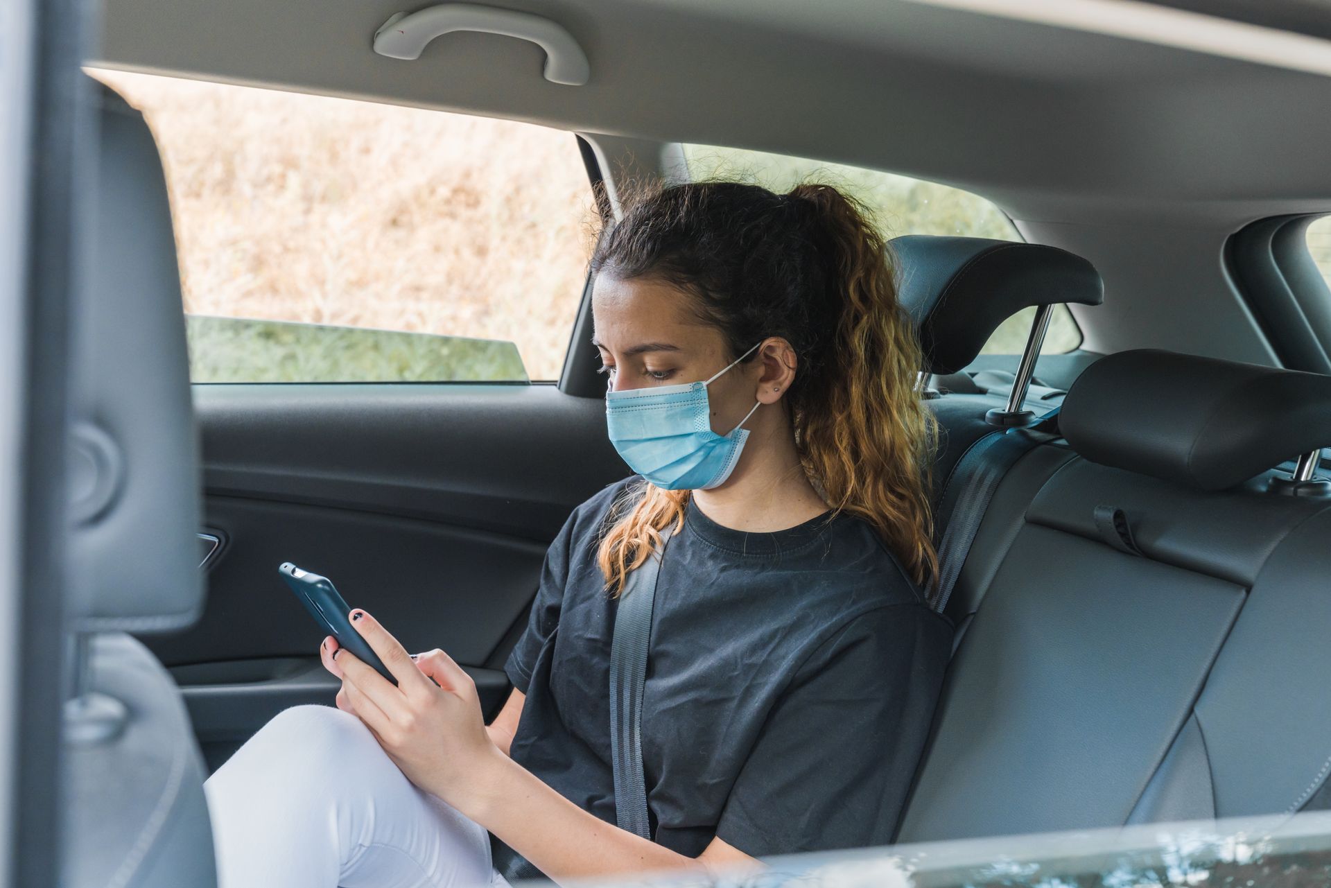 Passager masqué utilisant un smartphone sur la banquette arrière d'une voiture.