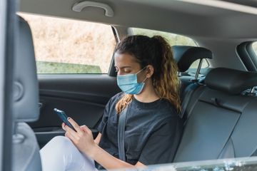 Une personne portant un masque utilise son téléphone sur la banquette arrière d'une voiture.