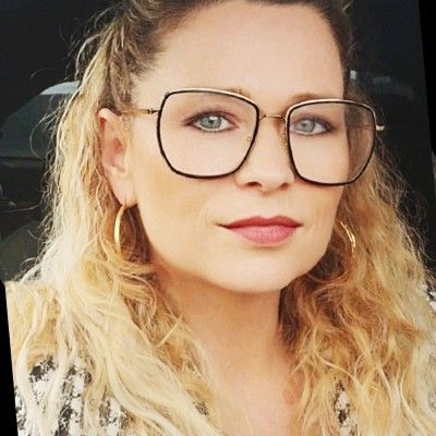 Portrait rapproché d'une personne portant de grandes lunettes et des créoles, faisant face à l'objectif avec une expression neutre.