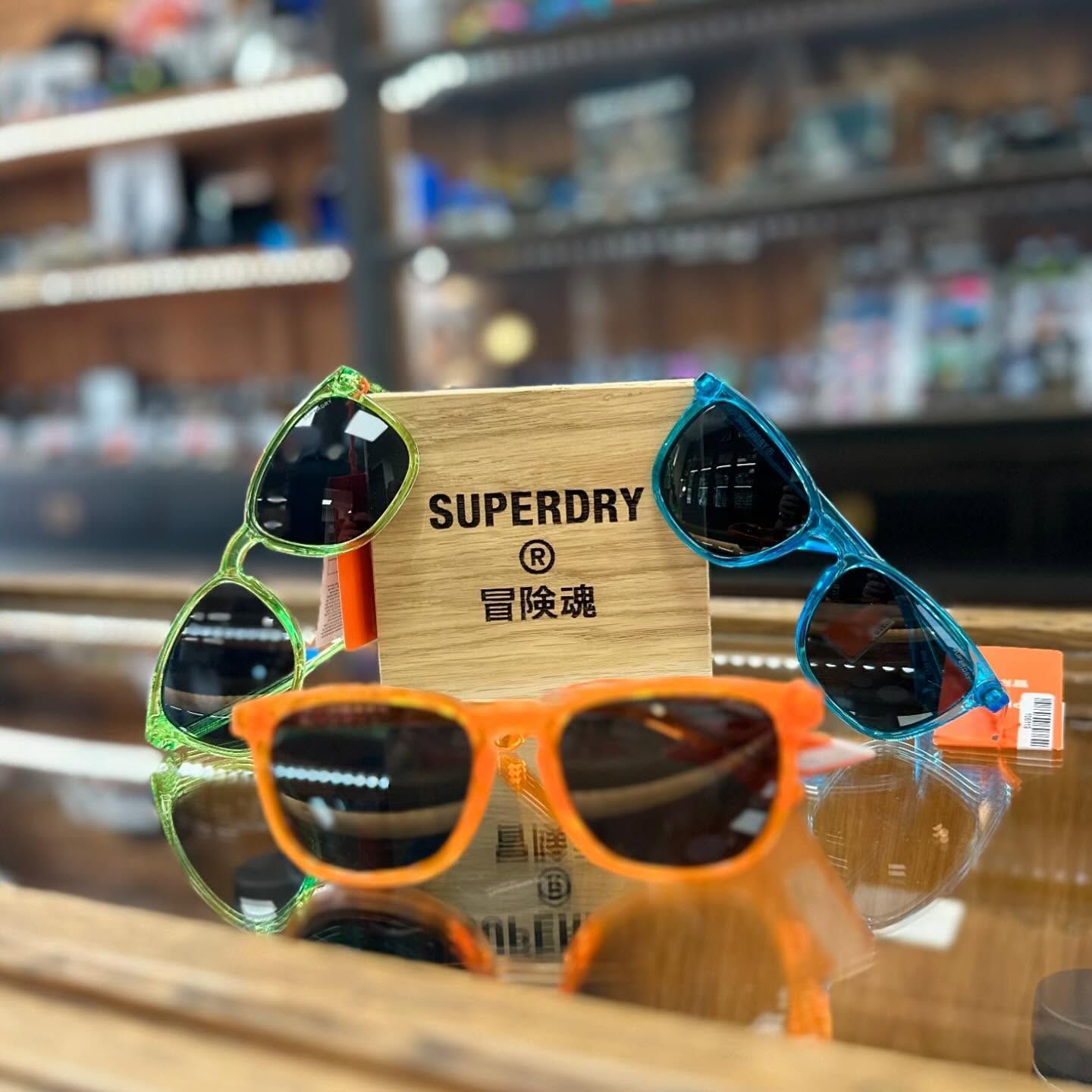 Trois paires de lunettes de soleil de la marque Superdry aux couleurs vives.