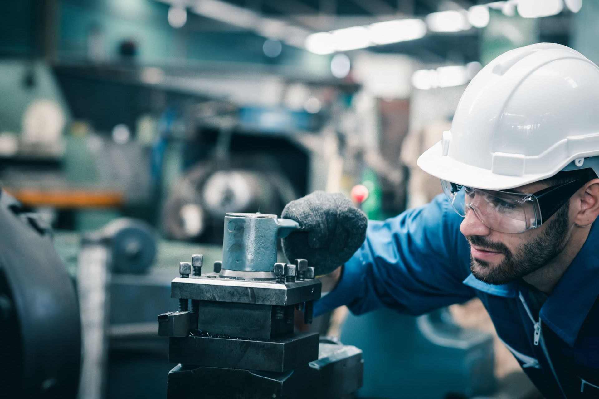 Un hombre que lleva casco y gafas de seguridad está trabajando en una máquina en una fábrica.
