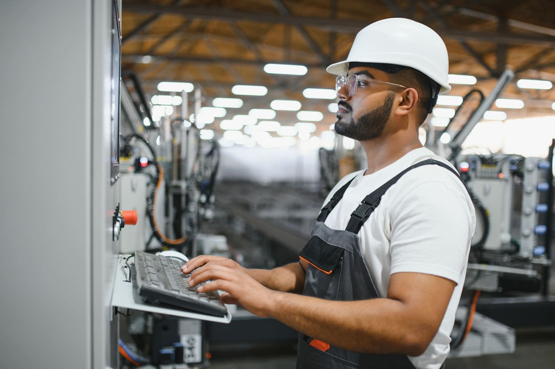 Un hombre que lleva casco y gafas de seguridad está trabajando en una computadora en una fábrica.