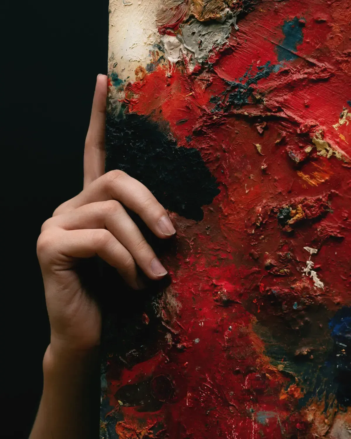 Una mano descansa sobre el borde de un lienzo texturizado pintado con gruesas y vibrantes