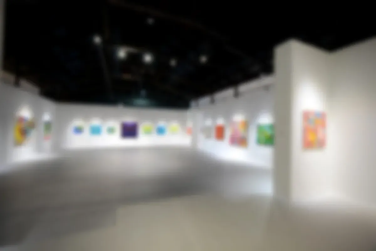 Una galería de arte bien iluminada exhibe coloridas pinturas sobre paredes blancas en un espacio limpio y abierto.