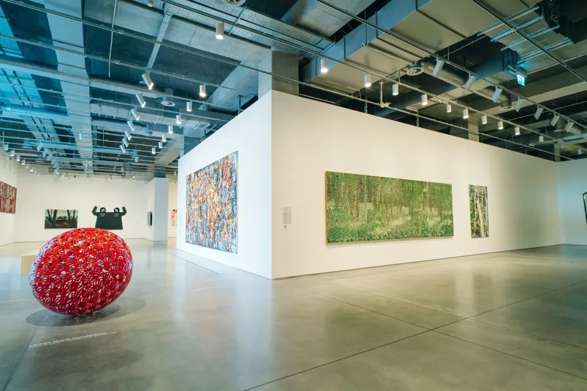 Una galería de arte moderna y luminosa, con pinturas en paredes blancas y una gran escultura esférica roja