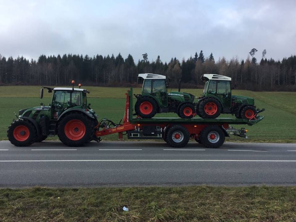 Un tracteur vert tire une remorque avec deux tracteurs verts plus petits sur une route.