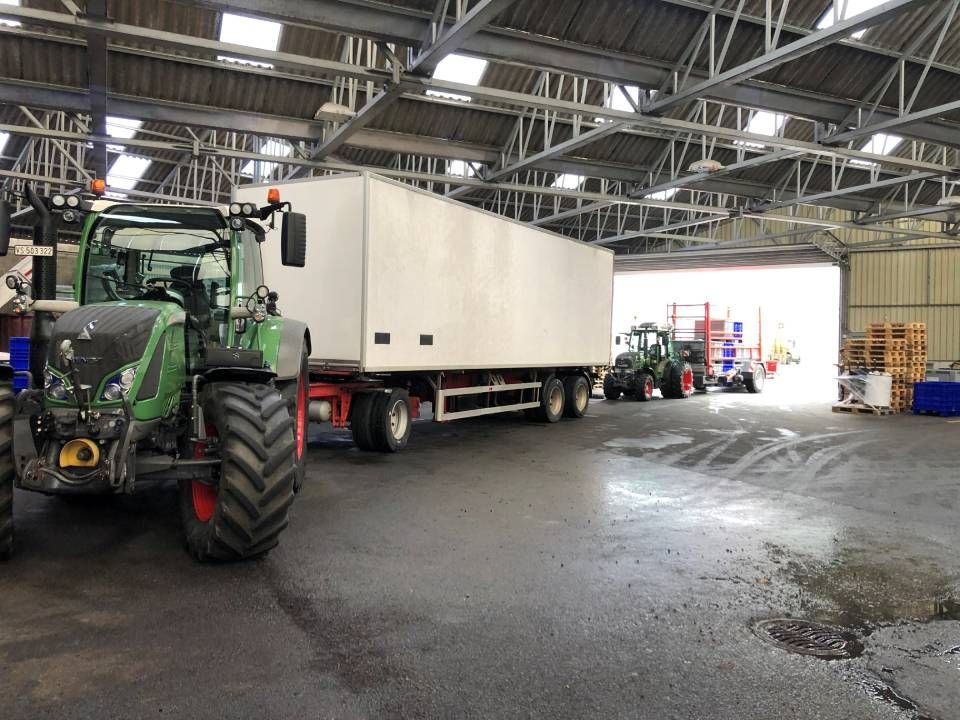 Un tracteur vert tire une grande remorque blanche à l'intérieur d'un entrepôt ; un autre tracteur est visible en arrière-plan.