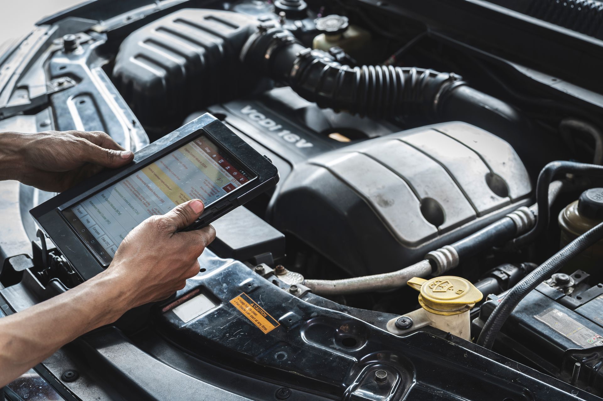 Mécanicien utilisant une tablette pour diagnostiquer un moteur de voiture dans un environnement bien éclairé.