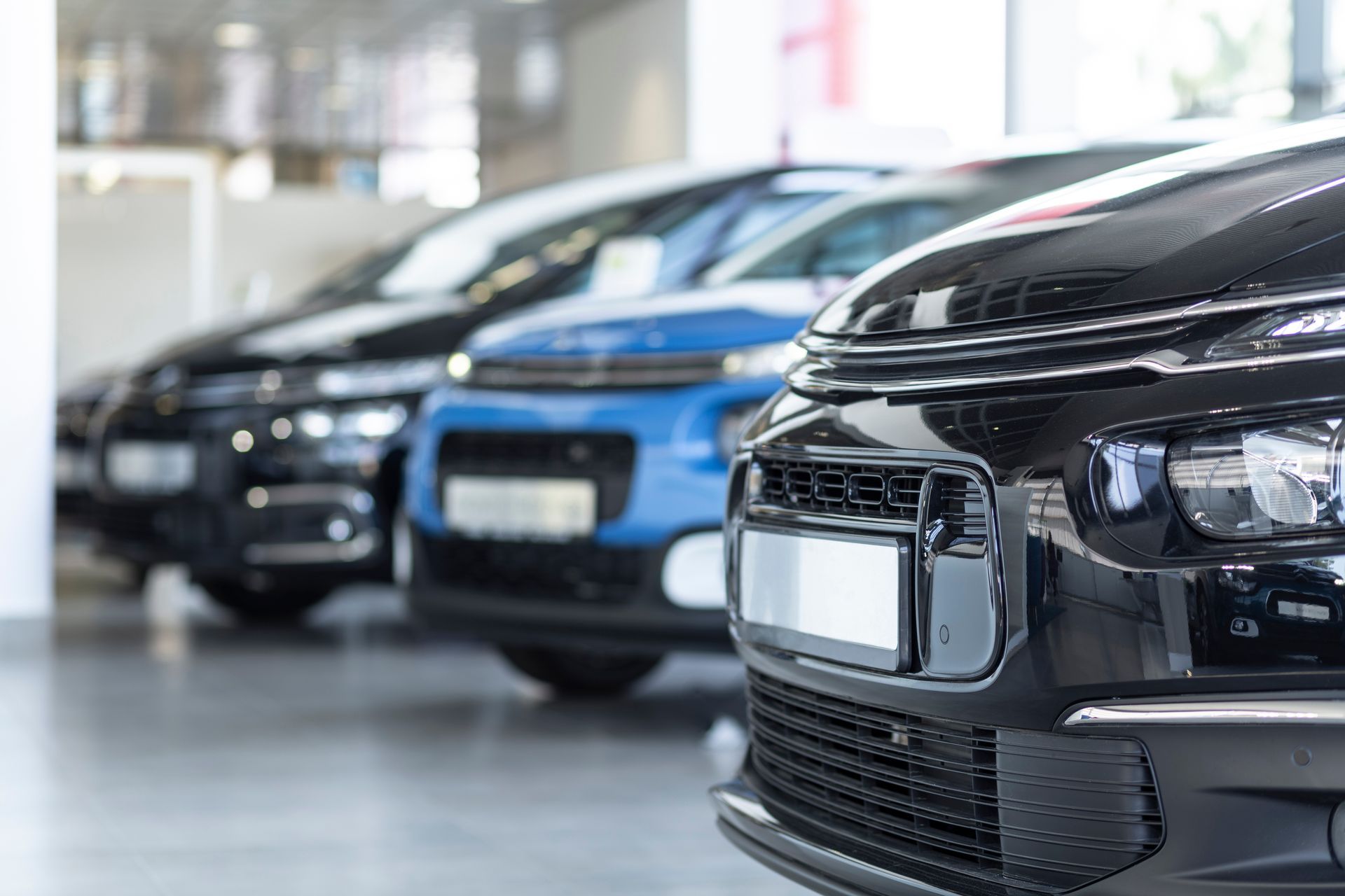 Voitures alignées dans une salle d'exposition, couleurs variées, focus sur l'avant de la voiture noire.