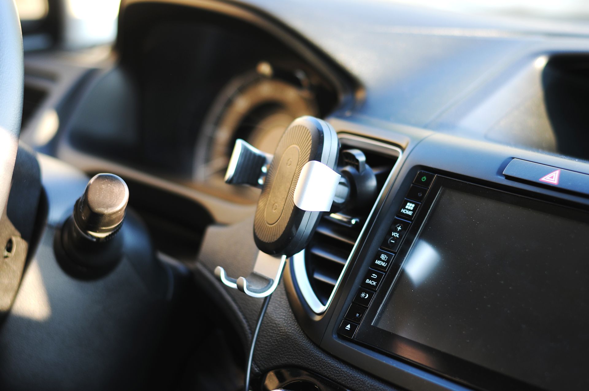 Un tableau de bord de voiture avec un support de téléphone monté sur la grille d'aération ; un volant à gauche.