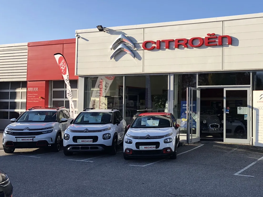 Concession Citroën avec trois voitures blanches et rouges garées à l'extérieur. Ciel dégagé, bâtiment avec logo.