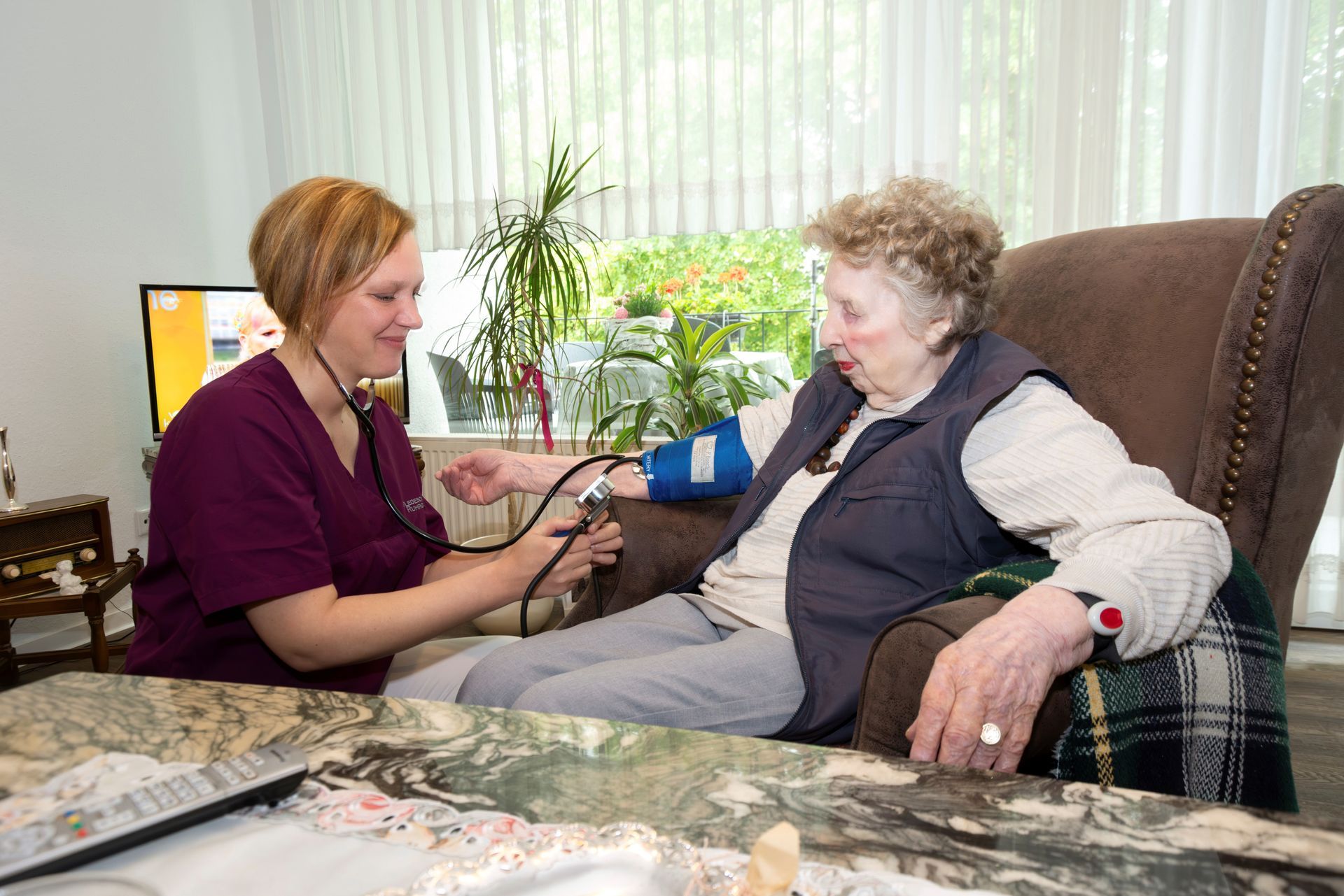 Eine Krankenschwester misst den Blutdruck einer älteren Person in deren häuslicher Umgebung.
