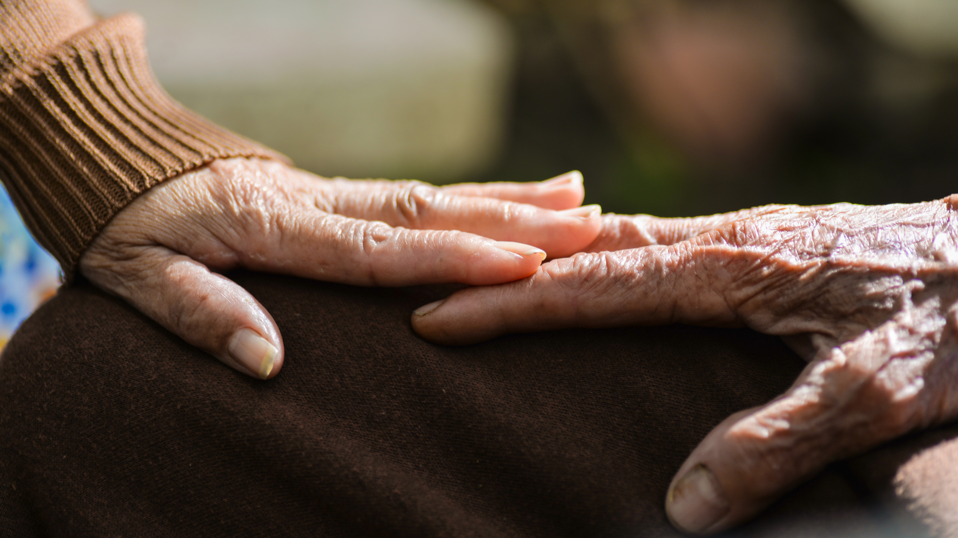 Zwei ältere Hände berühren sich sanft. Eine Hand liegt auf dem Handgelenk der anderen.