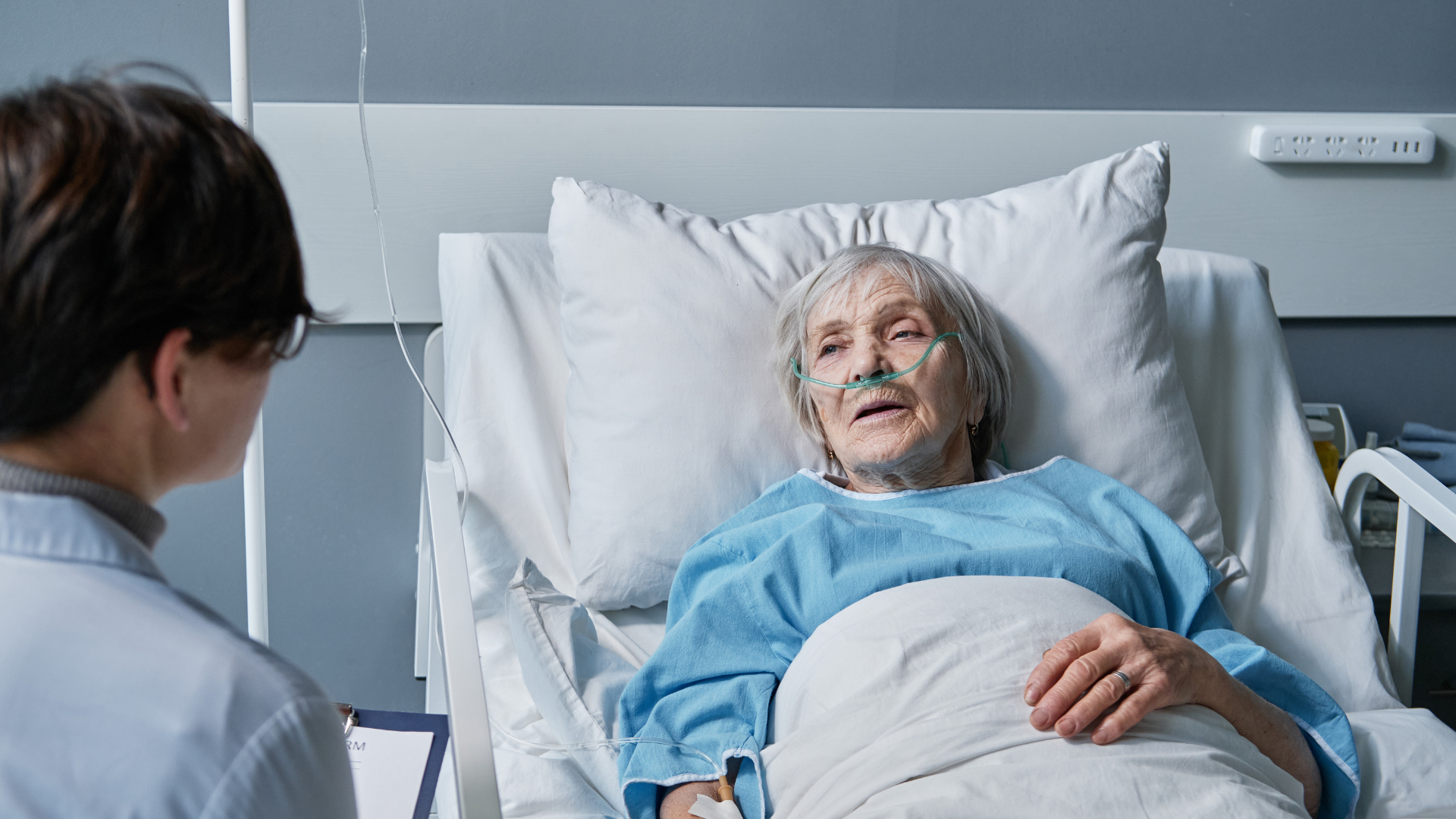 Hospital patient lying in bed while a clinician consults beside them