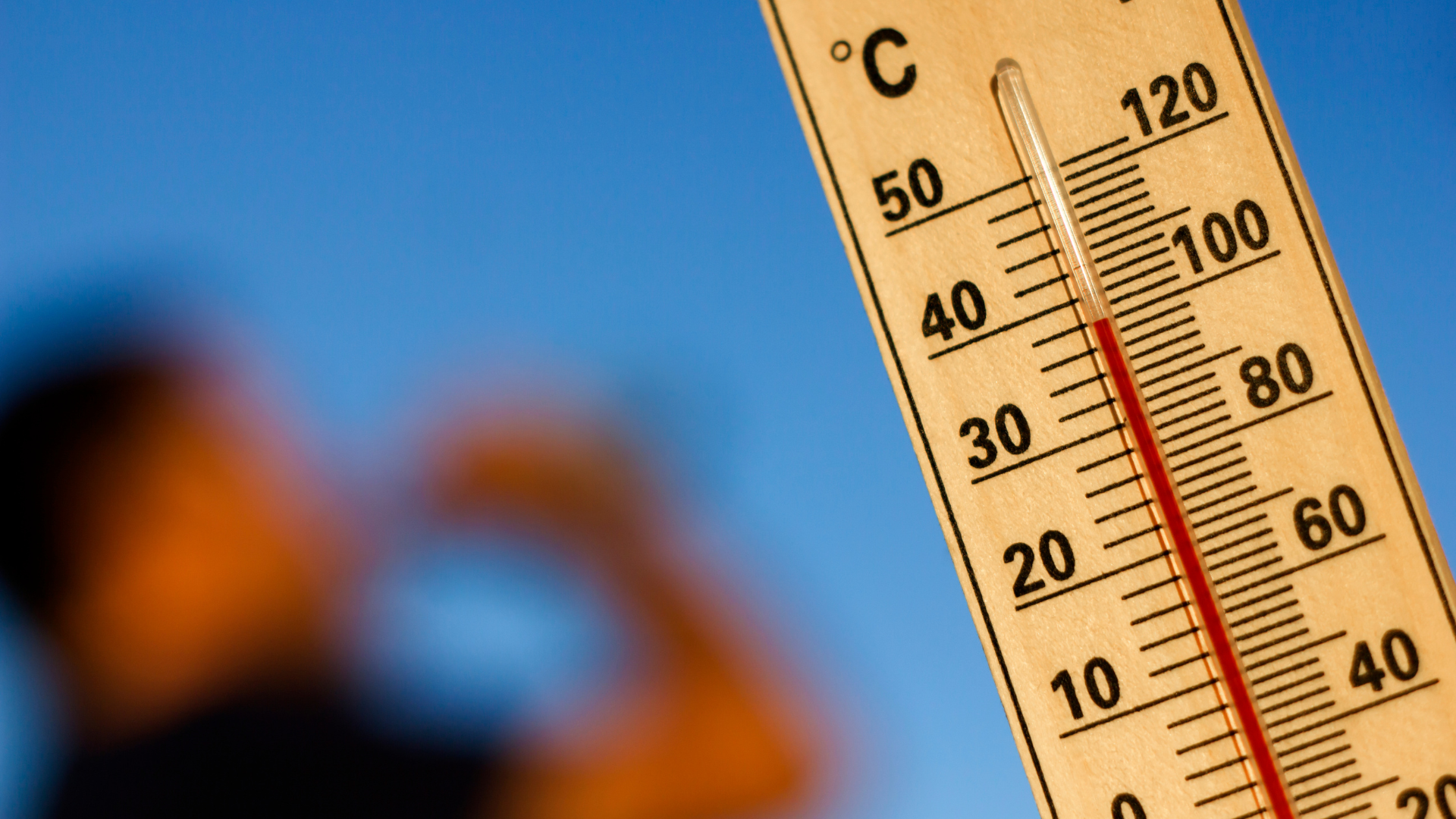 Thermometer, das eine hohe Temperatur anzeigt, mit einer unscharfen Person im Hintergrund