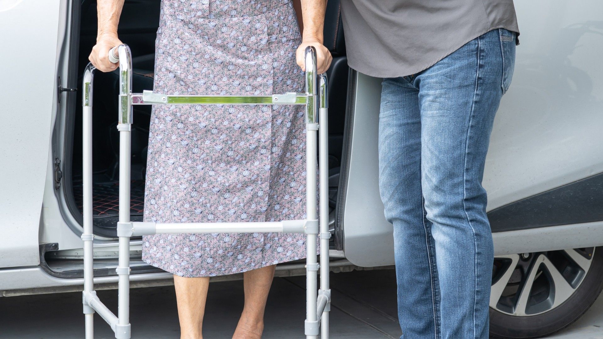 Zwei Personen: eine Frau am Rollator wird von pflegender Person unterstüzt