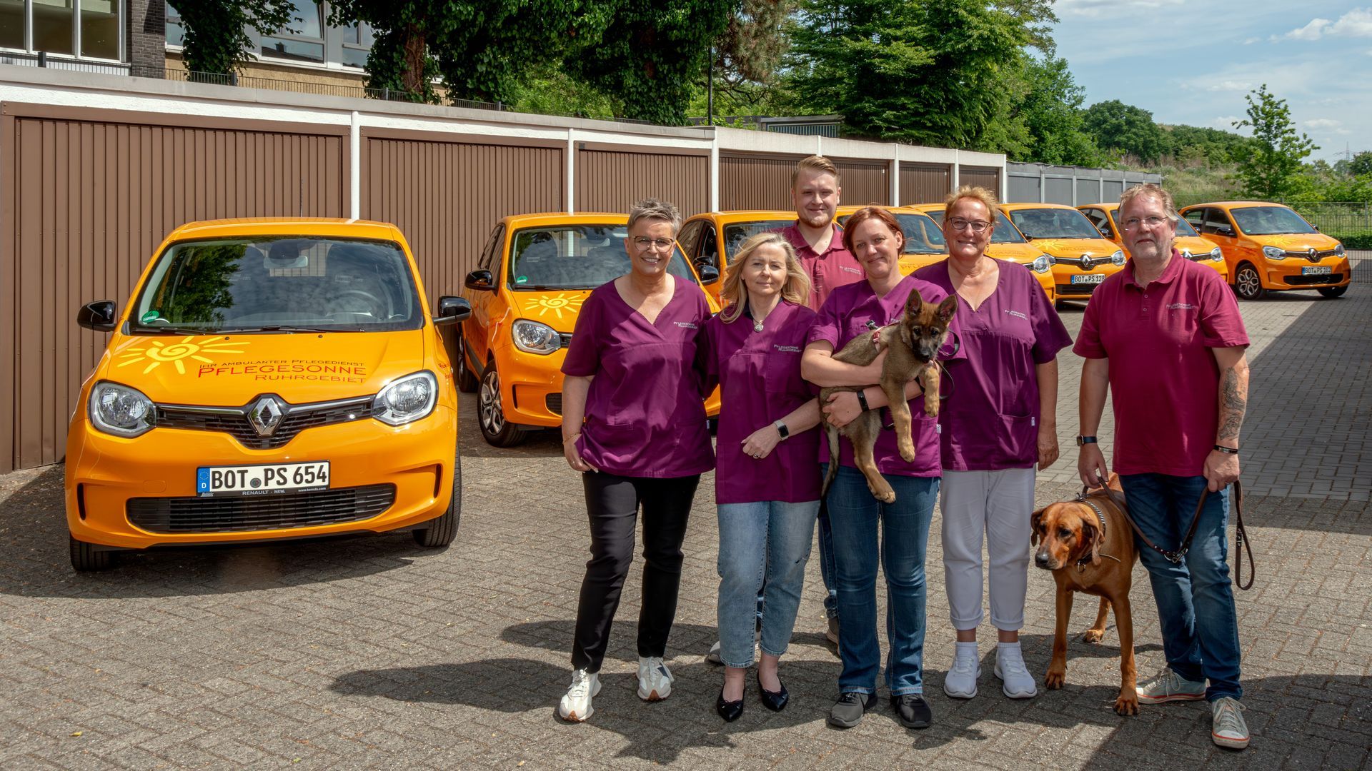 Eine Gruppe von Menschen in bordeauxroten Hemden mit orangefarbenen Autos und Hund