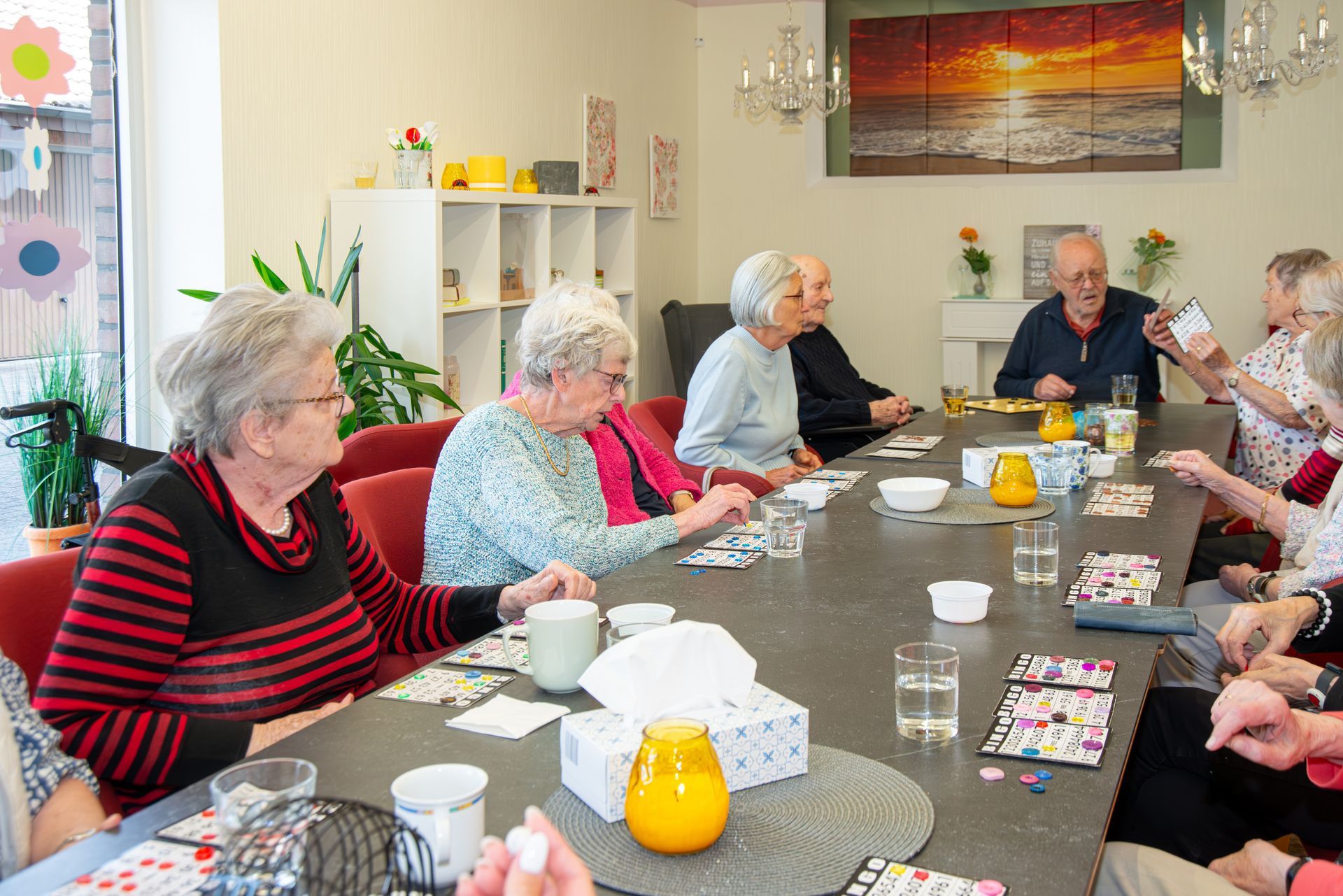 Senioren spielen an einem langen Tisch in einem gut beleuchteten Raum ein Spiel.
