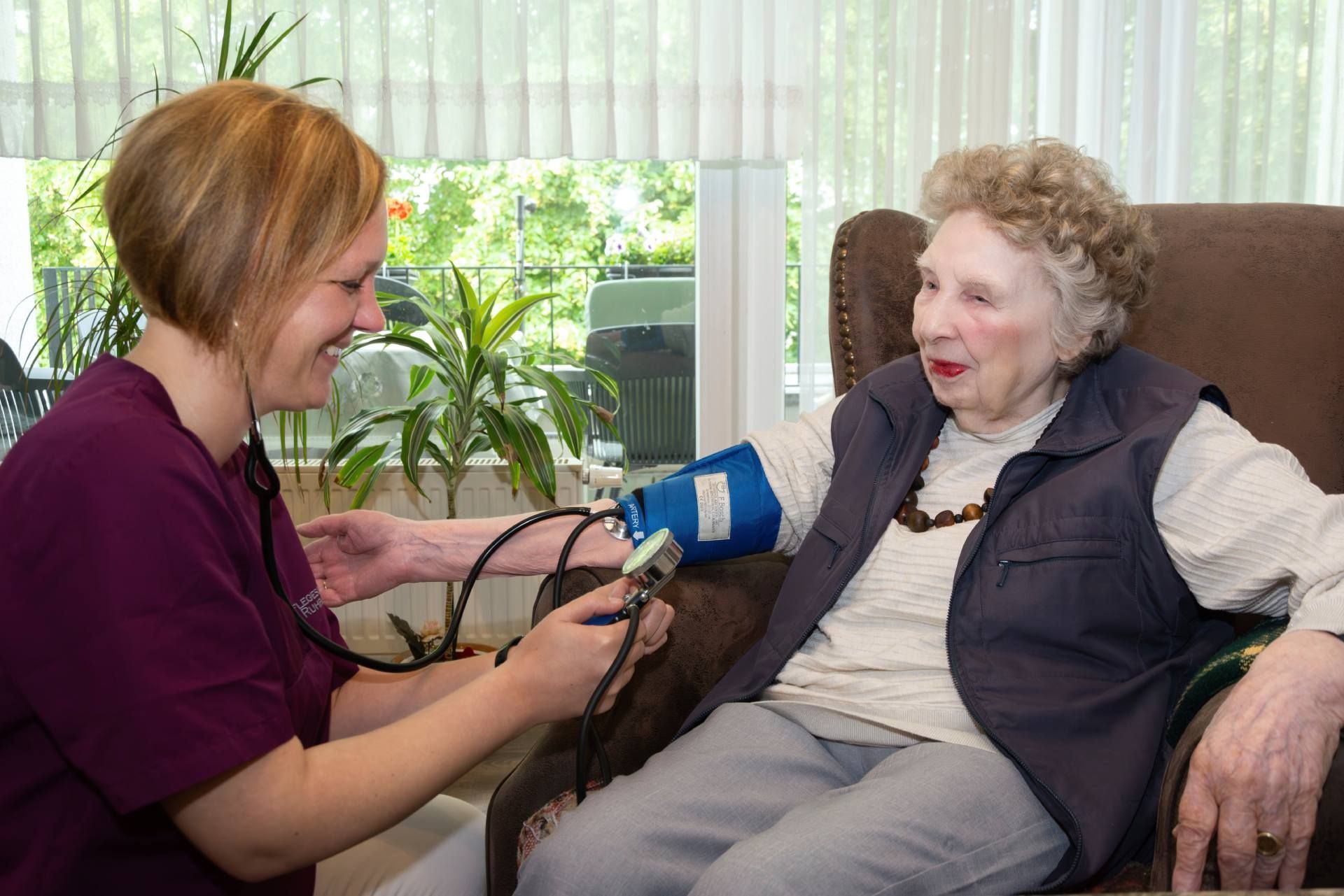 Pflege einer Rentnerin, bei der Blutdruck gemessen wird