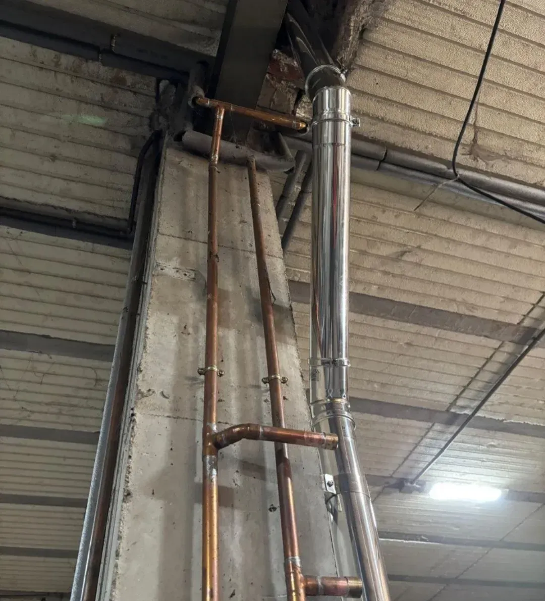 Techo industrial con tuberías de cobre y plata a la vista junto a una columna de hormigón.