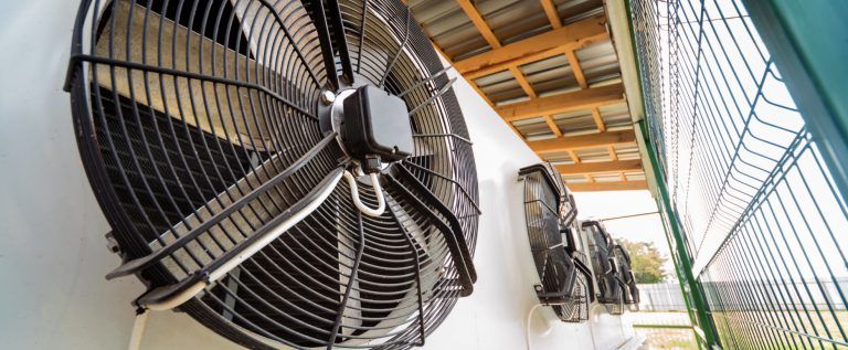 Grandes ventiladores industriales a lo largo de un pasillo cubierto en una fábrica o almacén.