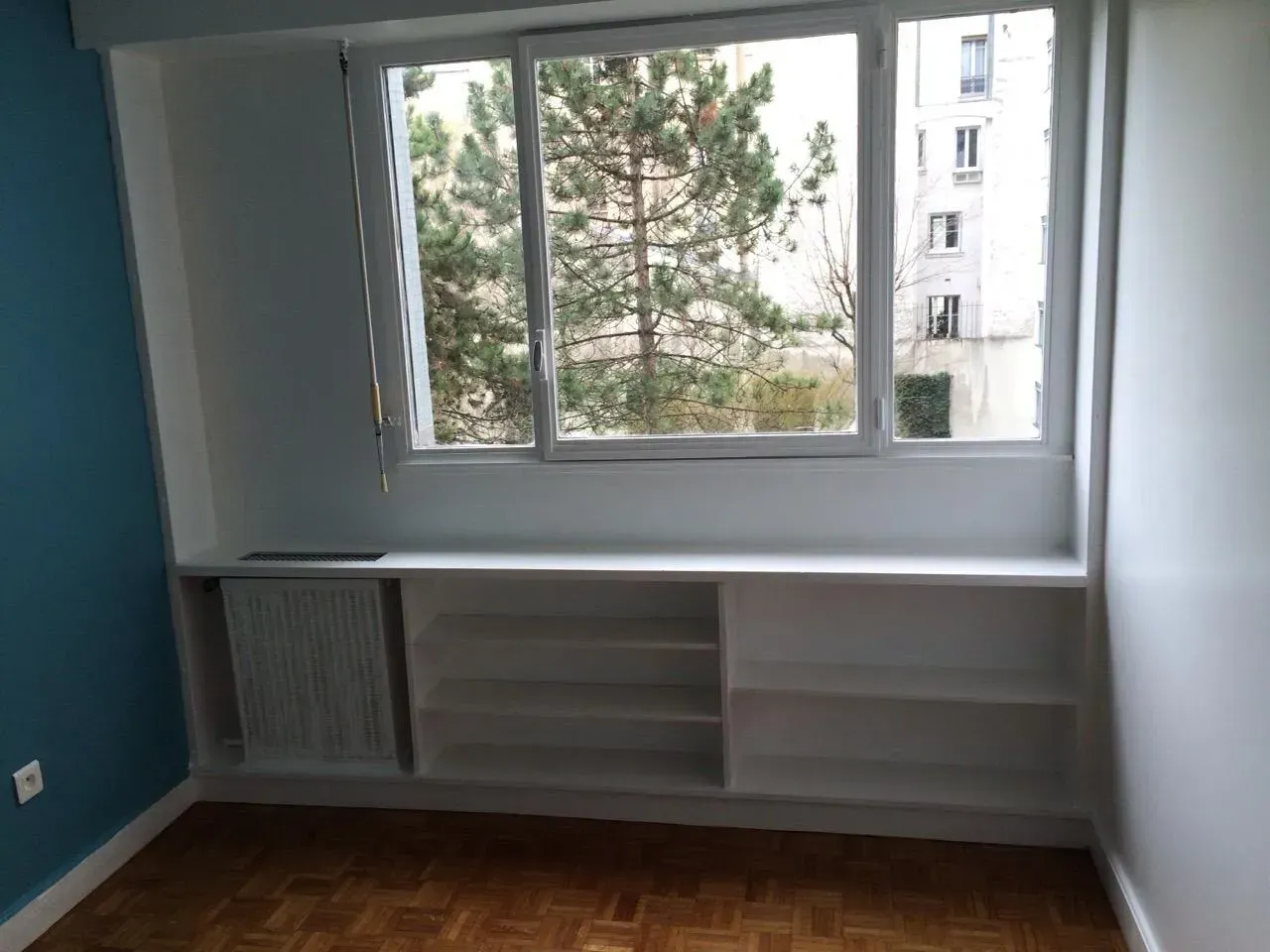 Chambre avec étagères blanches sous la fenêtre et des murs bleus