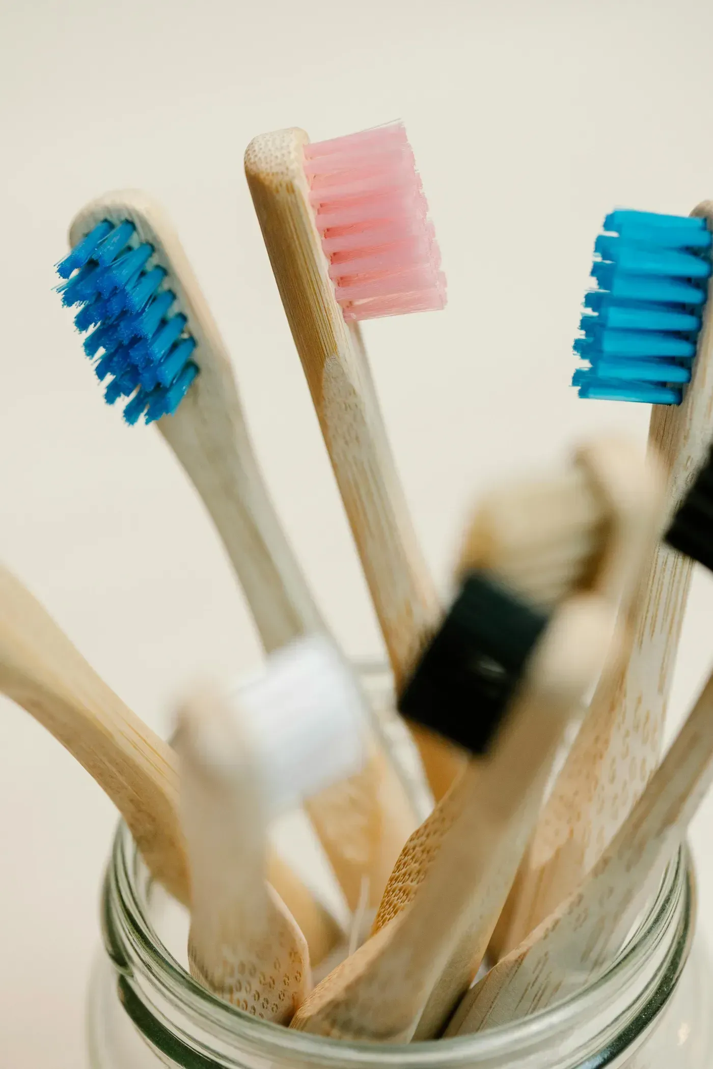 Cepillos de dientes de bambú con cerdas azules, rosas y beige en un frasco de vidrio.