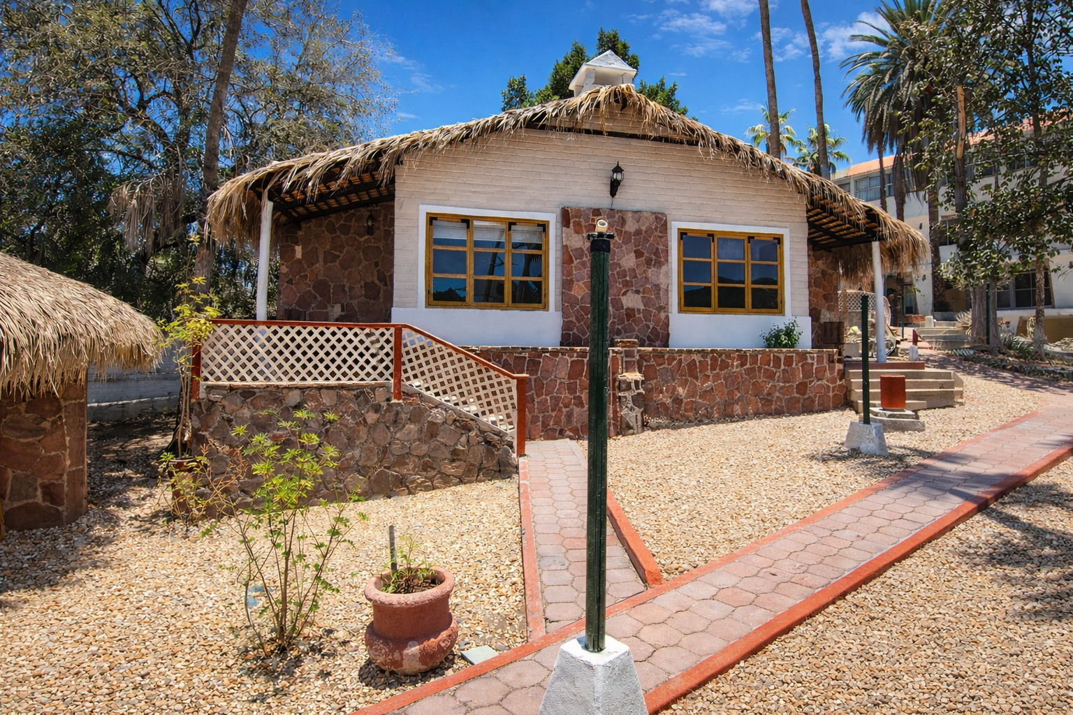 Una caba&ntilde;a de piedra con techo de paja y paredes de color tostado, situado en un paisaje soleado y des&eacute;rtico con un camino pavimentado.