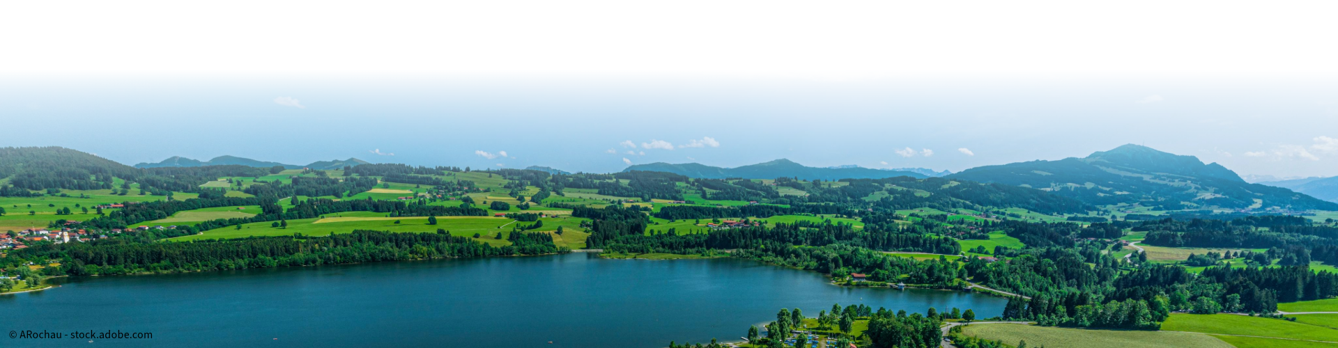Idyllische Seenlandschaft in Bayern mit grünen Hügeln und Bergen im Hintergrund, Naturkulisse für Erholung und Freizeit.