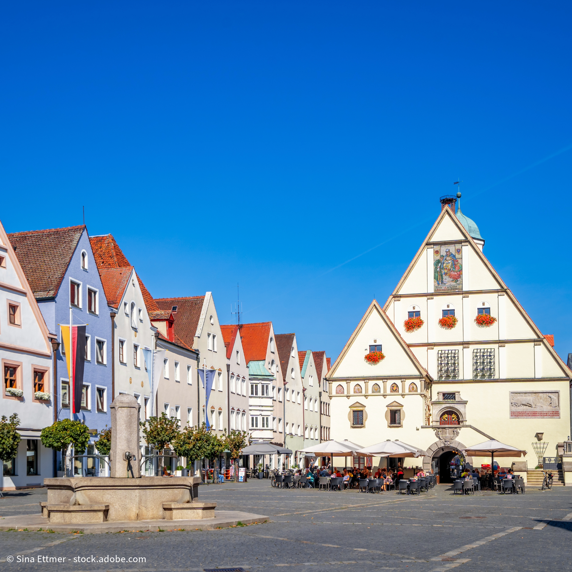 Historischer Marktplatz mit bunten Giebelhäusern, Rathaus und Straßencafés unter blauem Himmel in einer deutschen Altstadt.
