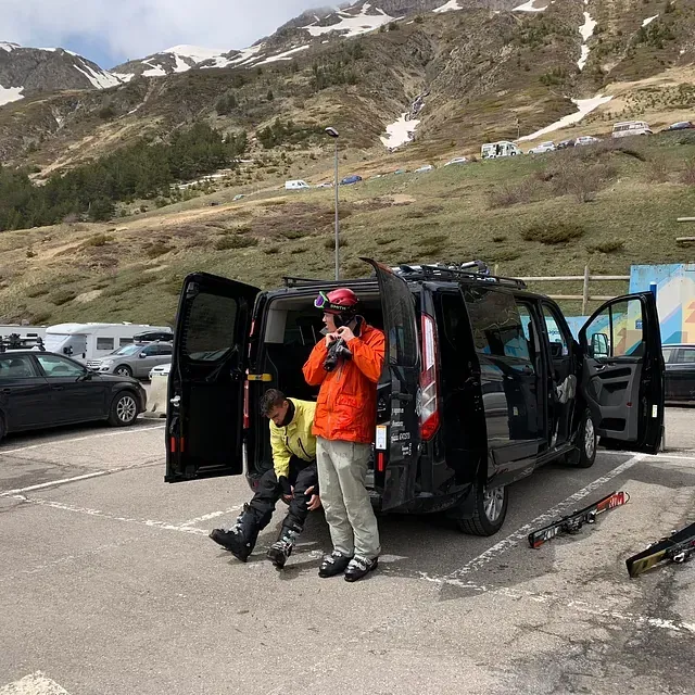 Un hombre con una chaqueta naranja está parado junto a una camioneta negra en un estacionamiento.