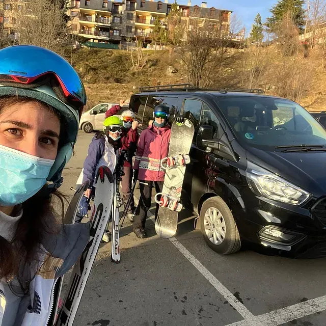 Una mujer con una máscara se encuentra junto a un grupo de personas que sostienen esquís y tablas de snowboard.