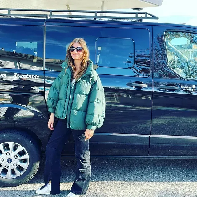 Una mujer con una chaqueta verde está parada frente a una camioneta negra.