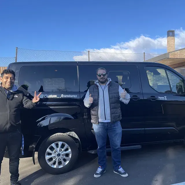 Dos hombres están parados al lado de una camioneta negra y hacen gestos de aprobación con los pulgares.