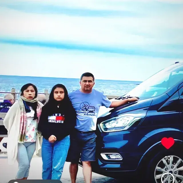 Un hombre y dos niñas posan frente a una camioneta azul.