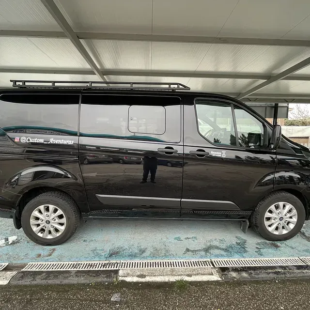 Una camioneta negra está estacionada en un estacionamiento bajo un toldo.