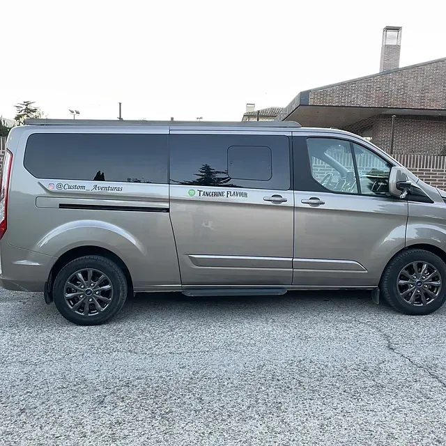 Una camioneta plateada está estacionada en un estacionamiento de grava frente a un edificio.