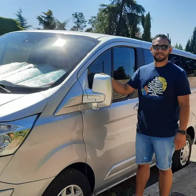 Un hombre con una camisa azul está de pie junto a una camioneta plateada.